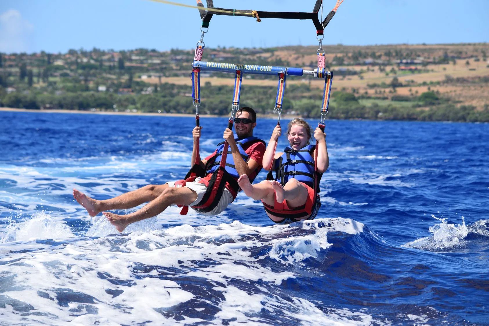 Two flyers laughing as the boat lowers them for a dip, feet dragging through the wake off West Maui
